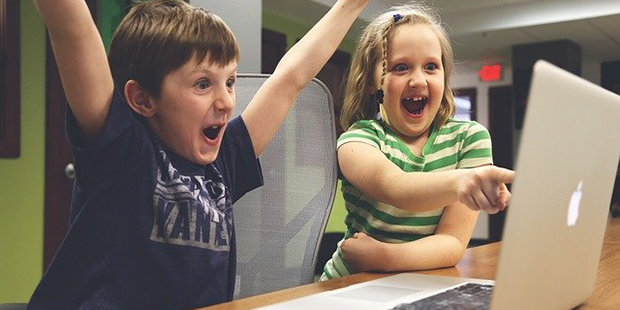 Närbild på två lyckliga barn som tittar och pekar mot en datorskärm.