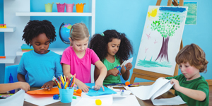 Fyra barn i förskoleålder målar och pysslar vid ett bord. 