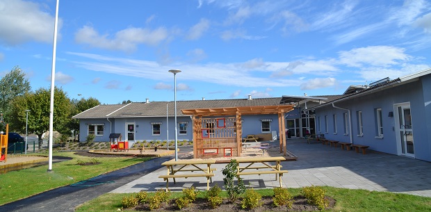 Bild på Borgens förskola. På bilden kan du se baksidan med lekredskap, blå fasad på huset och bord. 