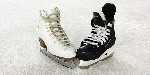 Låg vinkel vy på nedredelen av en ishockeyspelares kropp, hockestick och puck på isbanan.