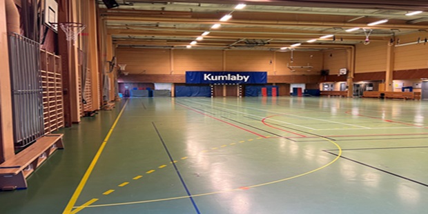 Bänkar, basketkorgar och längst bort i hörnet står det Kumlaby ovanför målet och på vardera sida av målet står det både små och störa gymnastikmattor