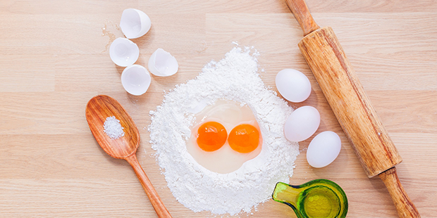 Bilden visar en bänksiva med mjöl, ägg, en kavel, slev och ett decilitermått. 