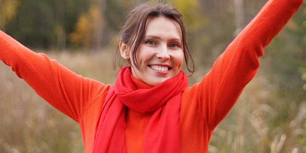 En glad kvinna i röd tröja som sträcker armarna mot skyn. 