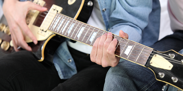Bilden visar en persons händer som spelar på en gitarr