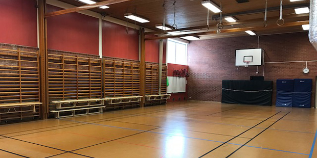 Bänkar, basketkorg och gymnastikmattor i lilla hallen. 