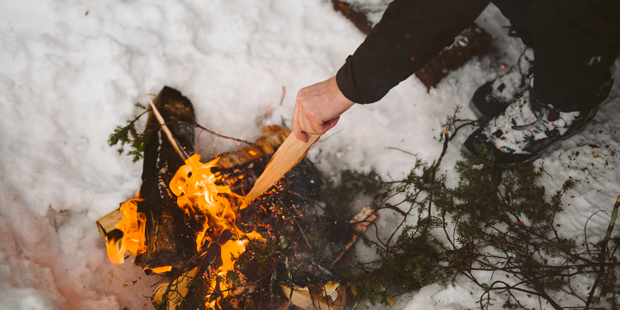 En person lägger ved på en eld ute i skogen.