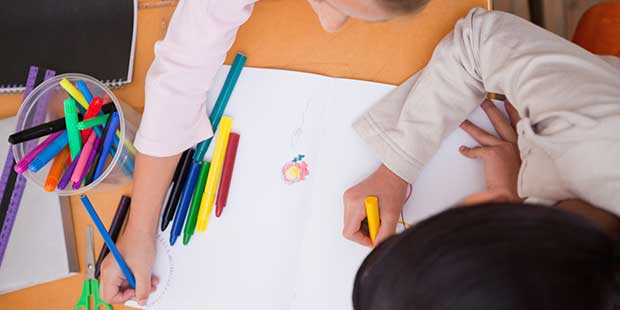 Bilden visar barn som ritar på papper med pennor