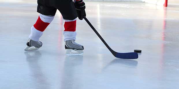 Låg vinkel vy på nedredelen av en ishockeyspelares kropp, hockestick och puck på isbanan.