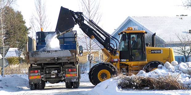 En maskin för snöröjning som lastar på snö på en lastbil i ett villaområde.