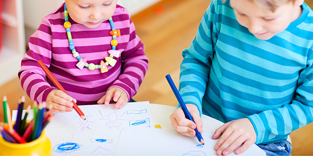 Bilden visar två barn som står vid ett bord och målar på papper 