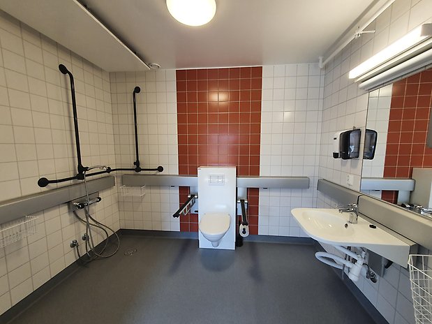 Stort kaklat badrum med handikappanpassad toalett, dusch och handfat.